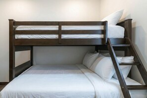 A bunk bed with a ladder, white bedding, and a wooden frame. - The Powder Den (Revelstoke)