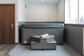 A spa room with a massage table, a bench, and a window. - The Powder Den (Revelstoke)