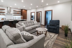 A modern living room with a grey sofa set, a round coffee table, and a blue armchair. - The Powder Den (Revelstoke)