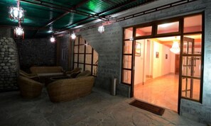 Una habitación con piso de piedra, muebles de mimbre, un amplio puerta corredera que da a otra estancia y lámparas colgantes.