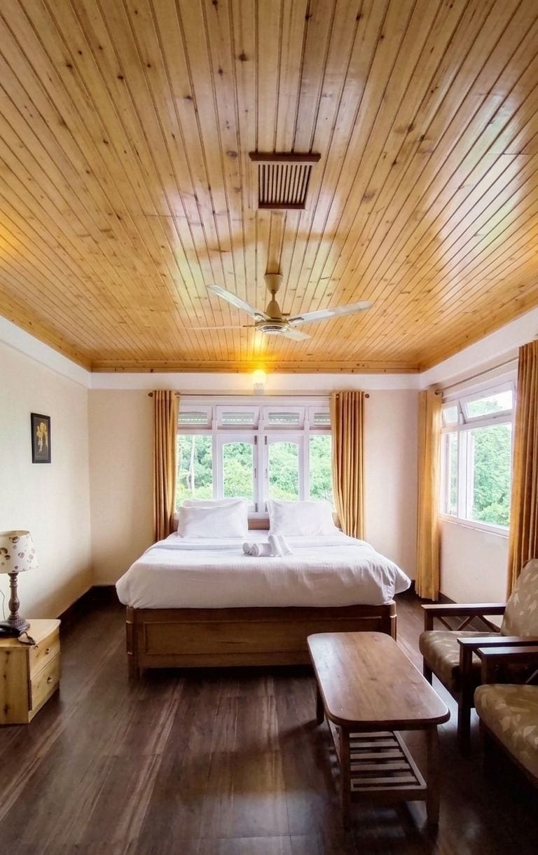 A room with a wooden ceiling, a bed, a bench, a table, and a chair.
