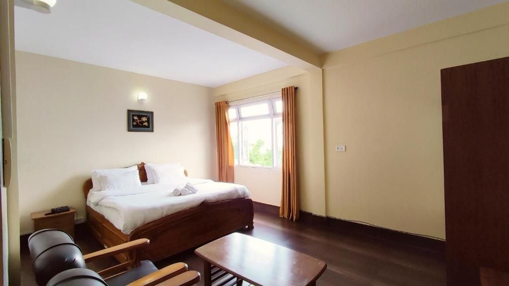 Ein Hotelzimmer mit Bett, Nachttisch, Stuhl und einem Fenster mit Vorhängen.