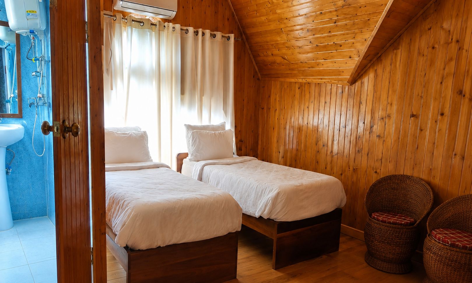 A wooden-paneled room with two beds, a bathroom with a sink, and a shower.