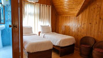 A wooden-paneled room with two beds, a bathroom with a sink, and a shower.