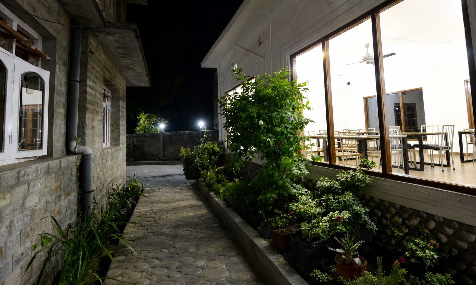 Un sendero de piedra que lleva a un edificio con un comedor visible a través de amplias ventanas.