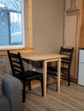 Ein kleiner Essbereich mit einem Tisch und zwei Stühlen, ein Fenster mit Blick auf verschneite Bäume und ein Holzschrank.
