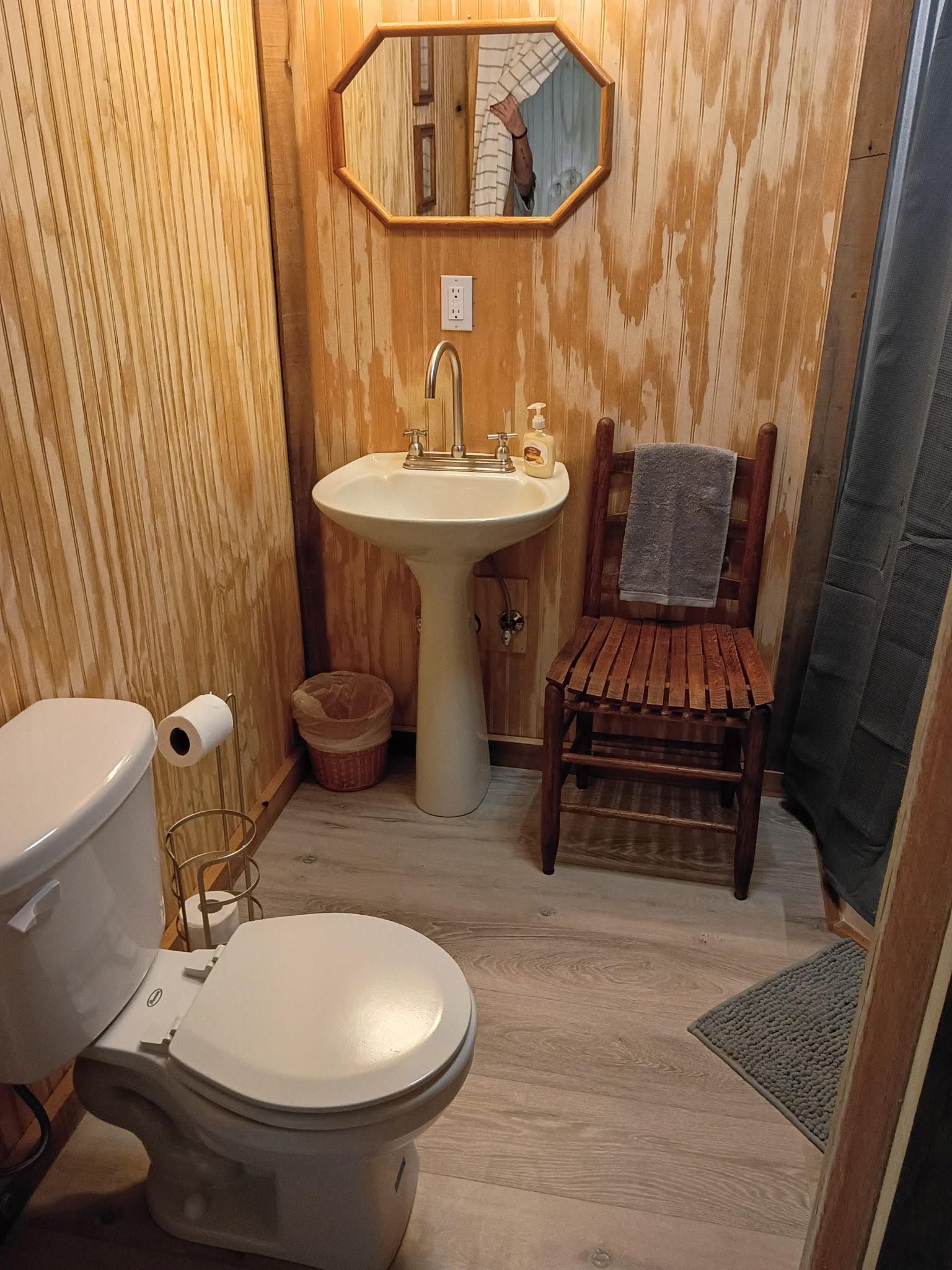 A bathroom with a toilet, sink, and wooden chair.