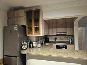 Une cuisine avec des meubles de rangement en bois, un réfrigérateur en acier inoxydable, une machine à café et une bouilloire posées sur le plan de travail.