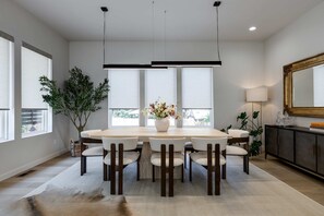 Ein Essbereich mit einem runden Tisch, Stühlen, einer Blumenvase und einem großen Spiegel an der Wand.