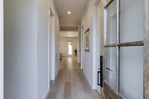 A hallway with a wooden floor, white walls, and a door with a glass panel. - The Eastside Darling - Modern 4BR w/ Fenced Yard, East Nashville 30+ Day Stay (Nashville)