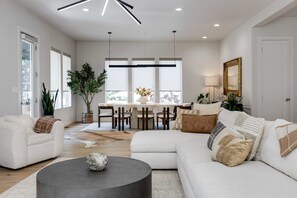 Ein geräumiges Wohnzimmer mit modernem Design, ausgestattet mit einem großen Sofa, einem Couchtisch und einem Essbereich mit Stühlen und Tisch.
