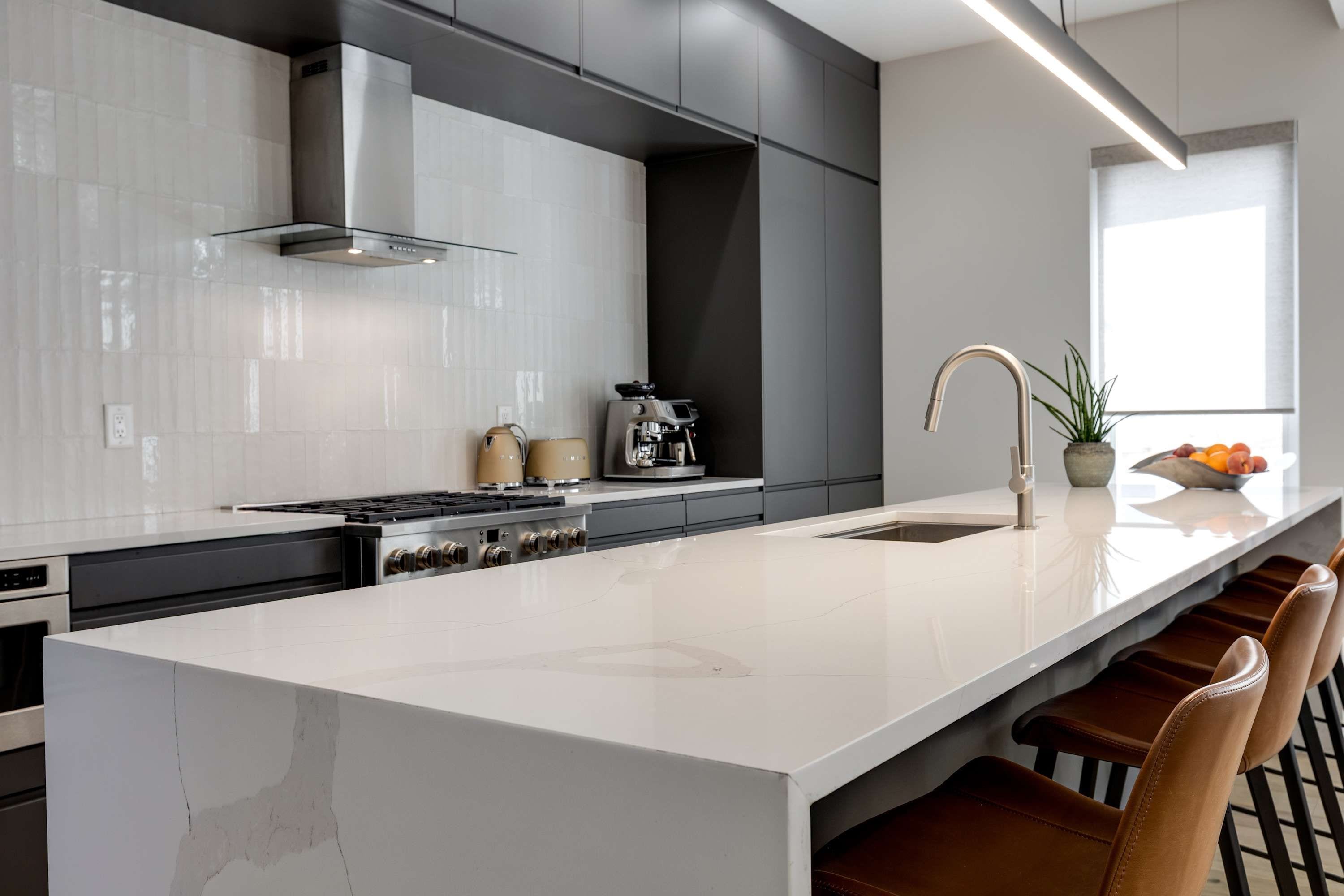 Une cuisine moderne dotée d’un grand îlot central, d’appareils électroménagers en acier inoxydable et d’un coin bar avec des tabourets en cuir.