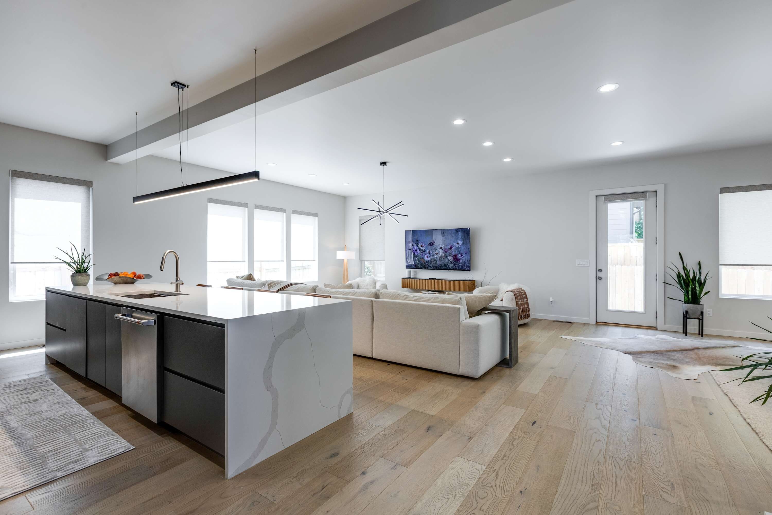 A modern kitchen with a large island, a dining area with a sofa, and a living room with a TV.