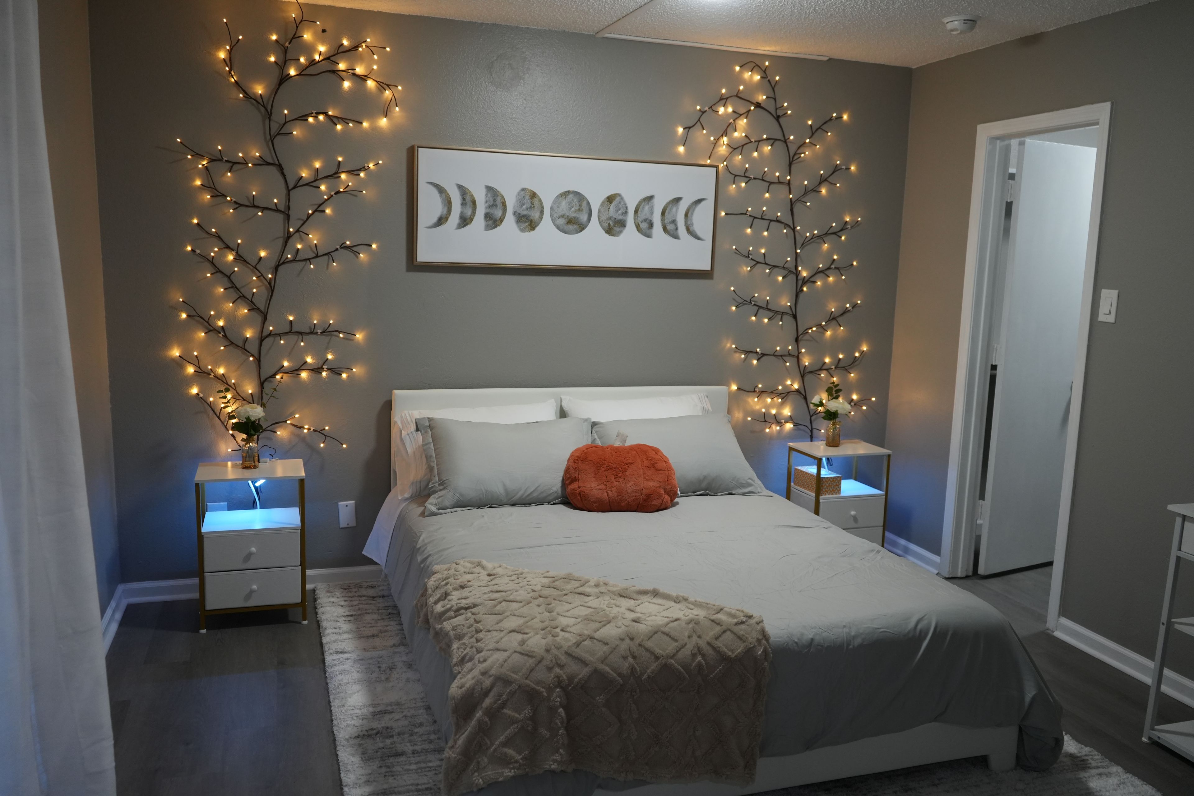 A bedroom with a bed, nightstands, a vase with flowers, and wall-mounted string lights.
