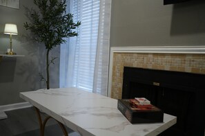 A room with a marble table, a fireplace with mosaic tiles, a potted plant, and a lamp. - 5 Min to Love Field-Comfy Studio with Free Parking. (Dallas)