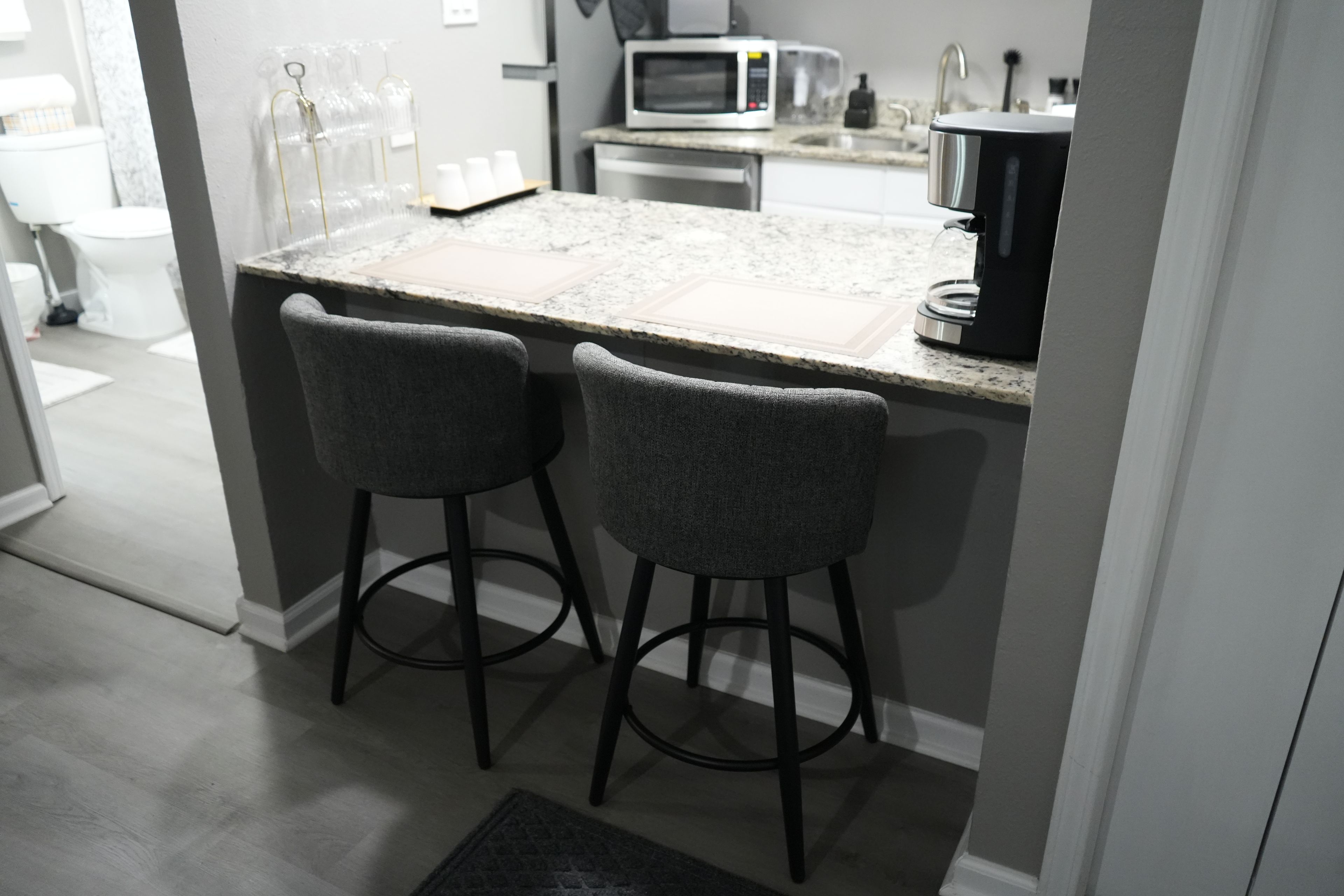A kitchen with a granite countertop, two bar stools, a microwave, and a coffee maker.