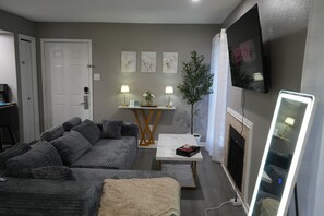 A modern living room with a grey sofa, a coffee table, a TV, and a fireplace. - 5 Min to Love Field-Comfy Studio with Free Parking. (Dallas)