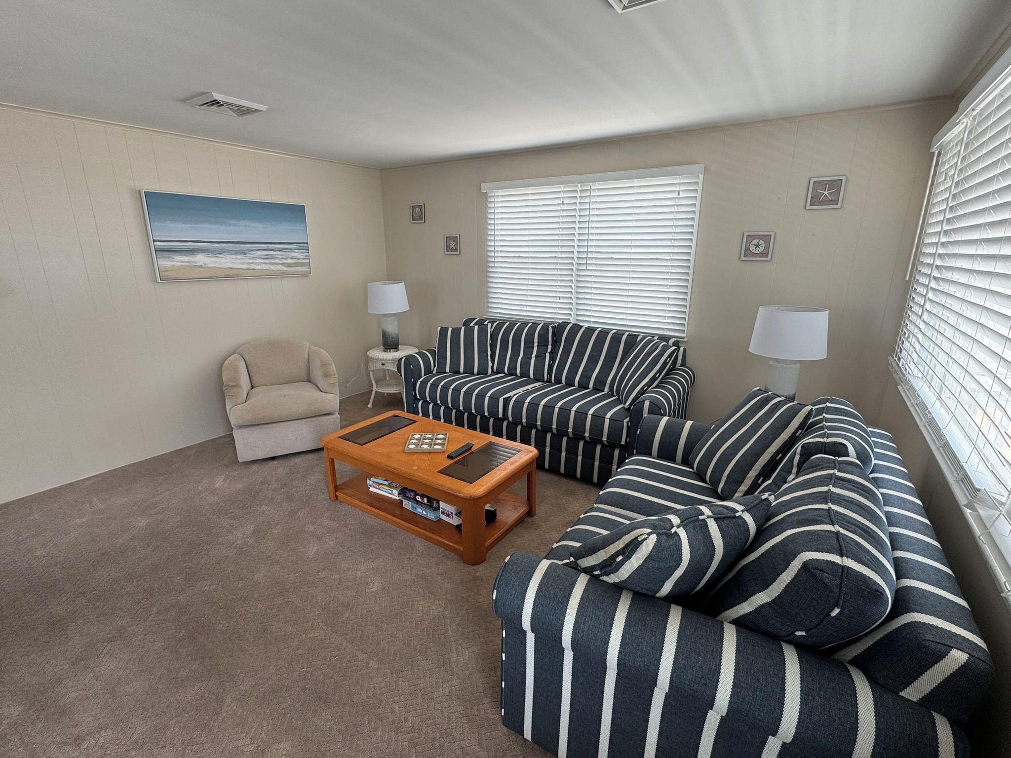 A living room with a sofa, a chair, a coffee table, and a window with blinds.