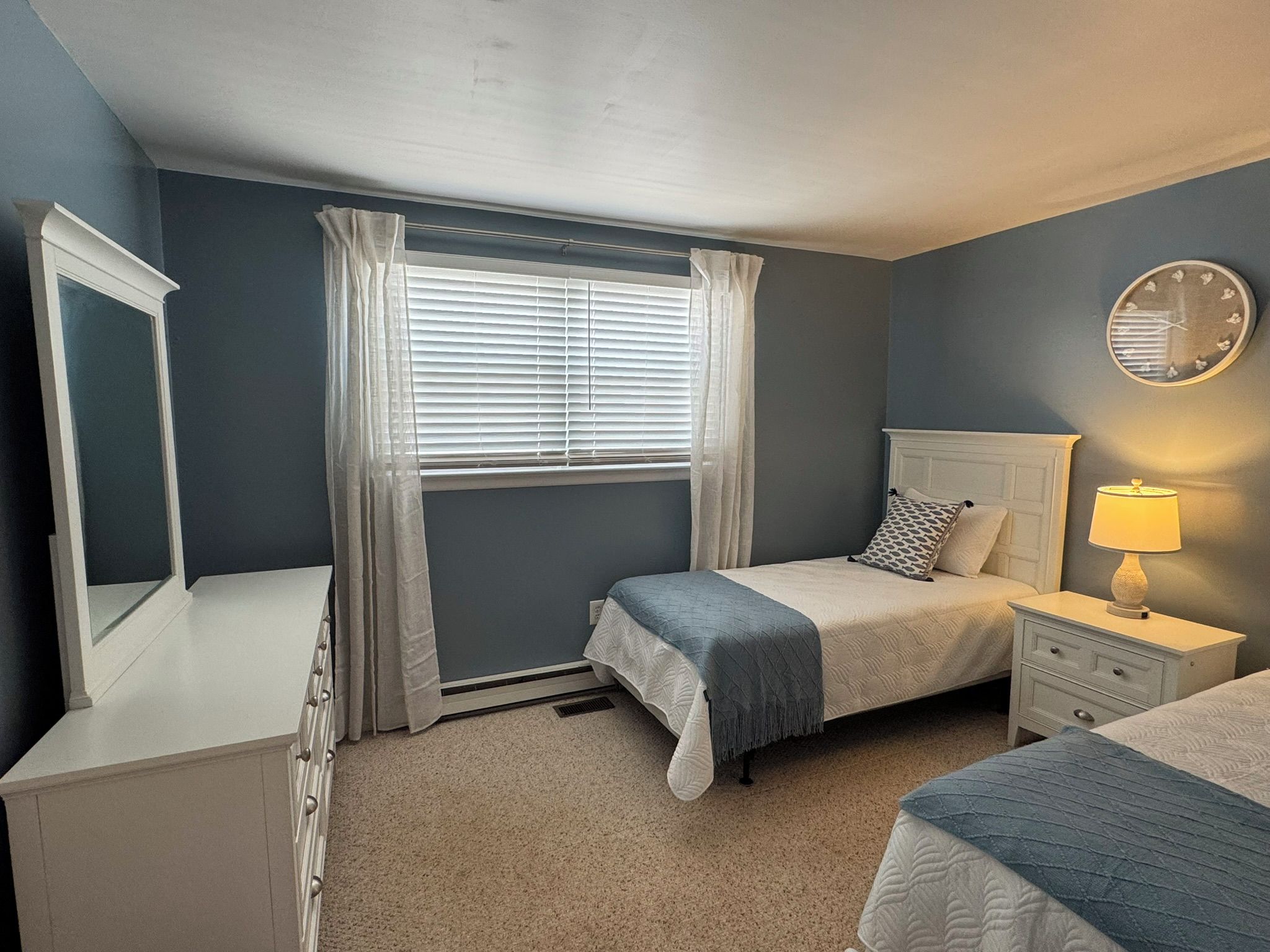 Un dormitorio con cama, mesitas de noche, un espejo y una ventana con cortinas.