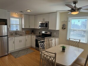 A modern kitchen with white cabinets, stainless steel appliances, and a dining area with a table and chairs. - Cozy Sea Isle City Beach Block Unit - 2nd Floor (Sea Isle City)