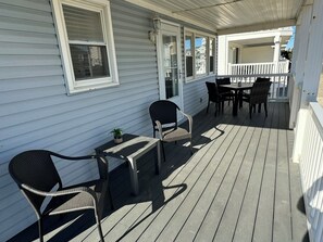 Eine überdachte Veranda mit Tisch und Stühlen, einem Blumentopf und Blick auf die Nachbarschaft.