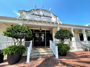 Ein Restaurant mit weißer Fassade, einem Schild mit der Aufschrift 'Tommy Bahama Restaurant | Bar | Store' und einem überdachten Eingang mit Stufen.