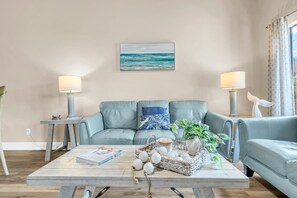 Un salon avec un canapé bleu clair, une table basse agrémentée d’objets décoratifs, un tableau encadré représentant l’océan et deux lampadaires.
