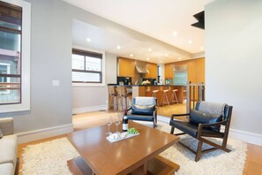 A modern living room with a wooden coffee table, two leather sofas, and a dining area with a kitchen in the background. - 4BR Ski Chalet, 2472 Sq Ft, w/ Pvt HotTub & Garage (Whistler)