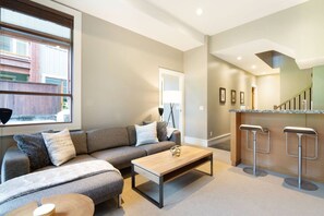 Una sala de estar moderna con un sofá modular, una mesa de centro y una zona de cocina con taburetes de bar.