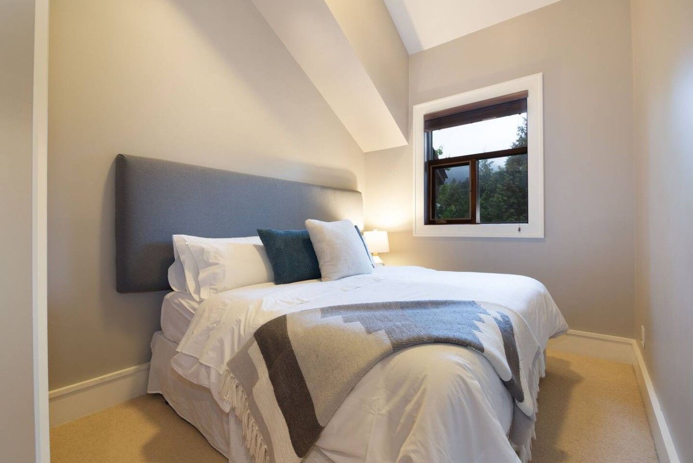 Un dormitorio con una cama, cabecera, ventana y mesita de noche.