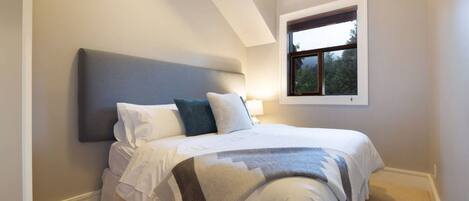 Un dormitorio con una cama, cabecera, ventana y mesita de noche.