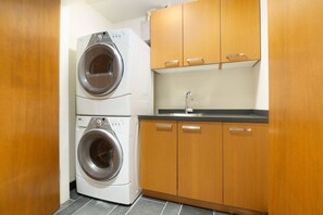 A compact kitchen with two stacked washing machines, wooden cabinets, and a sink. - 4BR Ski Chalet, 2472 Sq Ft, w/ Pvt HotTub & Garage (Whistler)