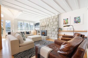 A modern living room with a stone wall, a fireplace, and a large window. - Stunning 4BR Chalet w/ Mountain Views, Pvt Garage (Whistler)