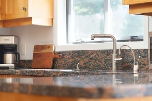 A kitchen with granite countertops, a coffee maker, a wooden cutting board, and a window above the sink. - Stunning 4BR Chalet w/ Mountain Views, Pvt Garage (Whistler)