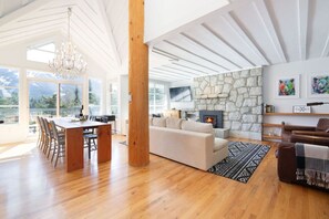 A spacious living area with a fireplace, a dining area with a wooden table, and a large window offering a view of the outdoors. - Stunning 4BR Chalet w/ Mountain Views, Pvt Garage (Whistler)