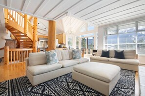 A spacious living area with a large sectional sofa, a wooden staircase, and a view of the outdoors. - Stunning 4BR Chalet w/ Mountain Views, Pvt Garage (Whistler)