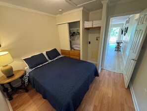 Een slaapkamer met een bed, nachtkastje, lamp en een inloopkast met kleding.