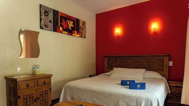 A hotel room with a bed, a wooden dresser, a table with a remote control, and a wall-mounted artwork. - Vrbo Property (Tepoztlan)