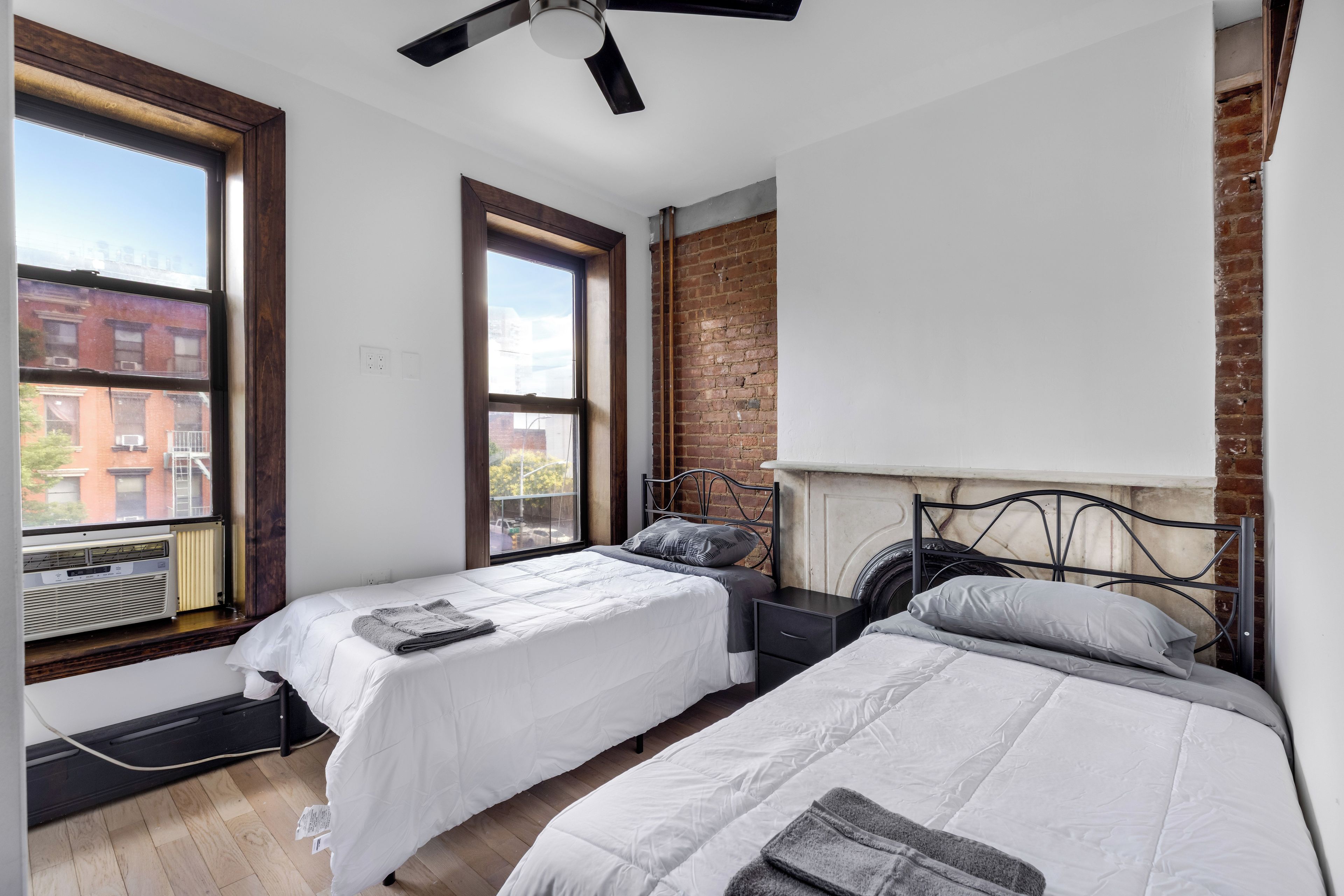 A bedroom with two beds, a brick wall, and a window.