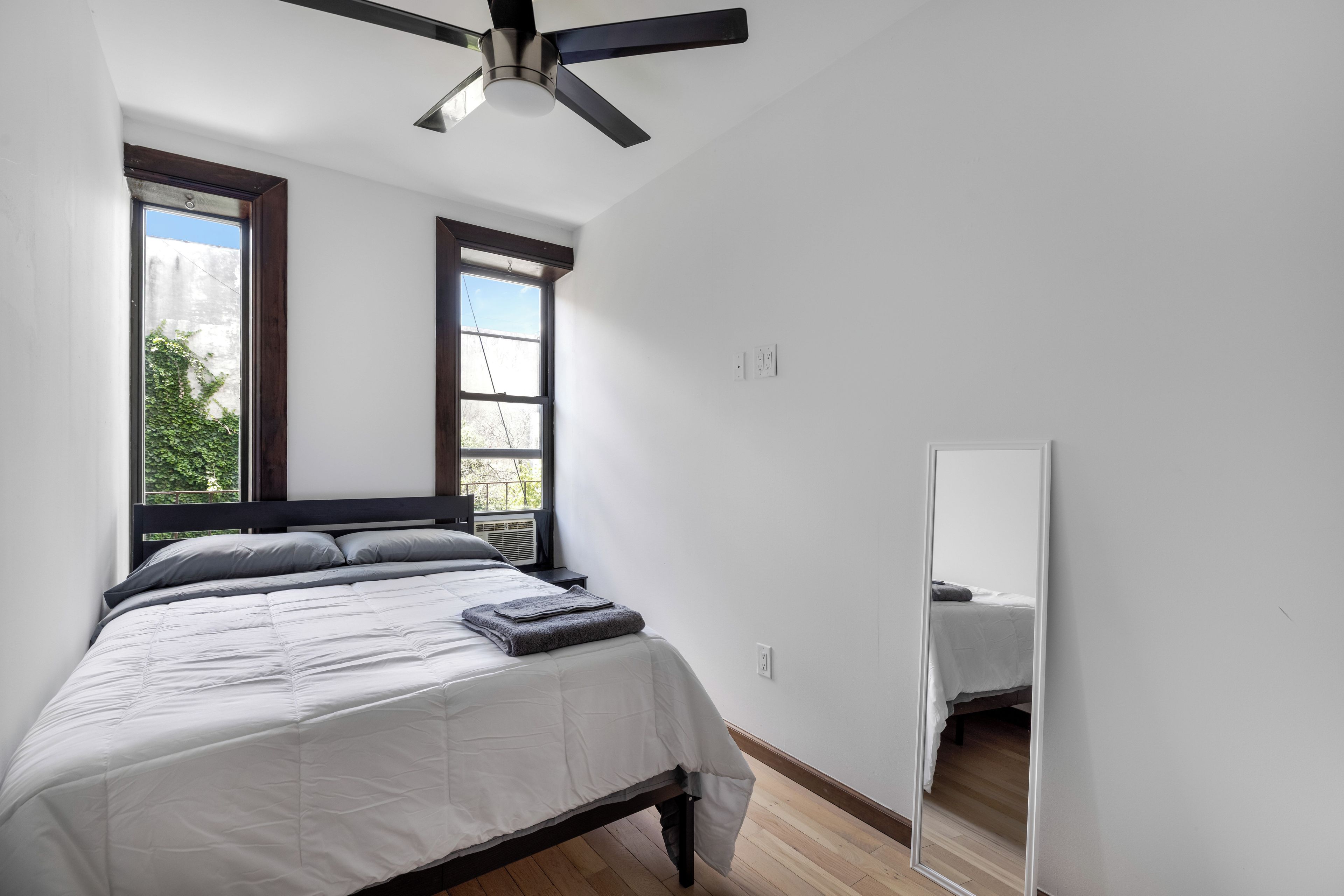 A bedroom with a bed, a ceiling fan, a window, and a mirror.