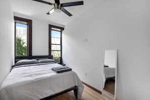 A bedroom with a bed, a ceiling fan, a window, and a mirror.