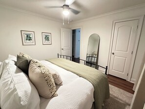 Een slaapkamer met een bed, een plafondventilator, twee ingelijste foto's en een deur.