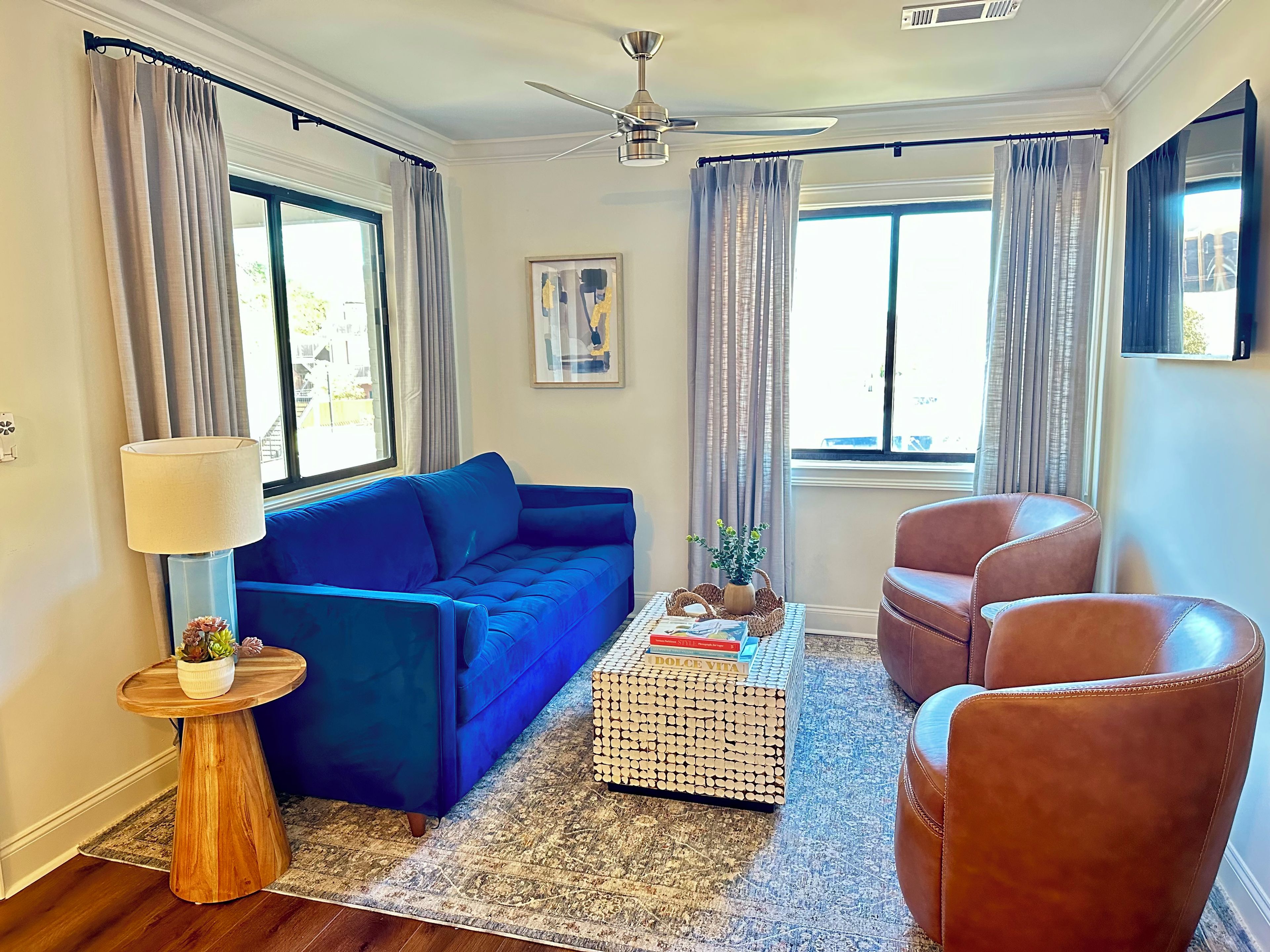 Una sala de estar con un sofá azul, un sillón de cuero marrón, una mesa redonda con libros y una lámpara de pie.