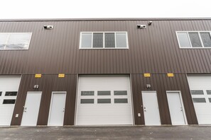 A multi-story industrial building with large garage doors and numbered windows. - The Alpine Den (Revelstoke)