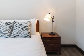 Ein ordentlich bezogenes Bett mit gemusterten Kissen, einer Nachttischlampe und einem Holennachttisch.