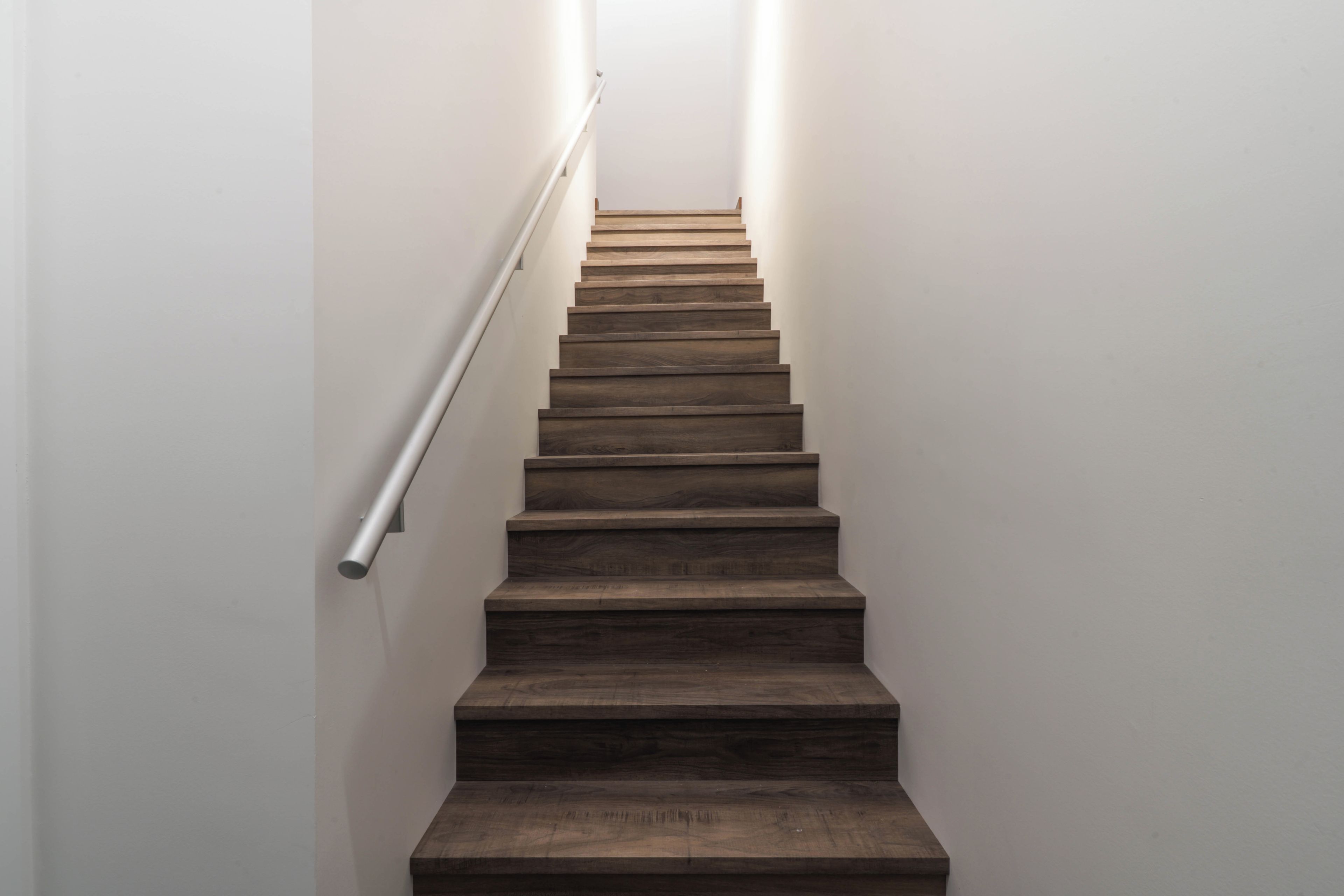 A wooden staircase with a handrail, leading upwards.