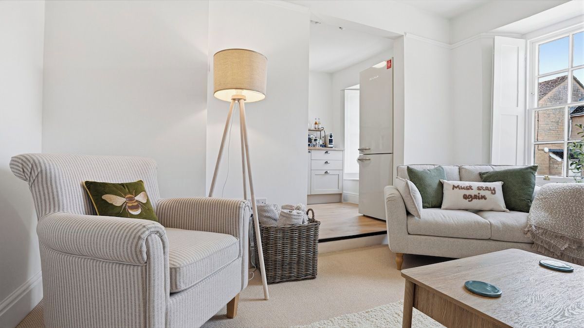 A modern living room with a striped armchair, a floor lamp, a sofa with green pillows, and a coffee table.