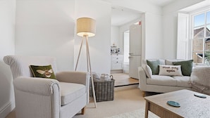 Uma sala de estar moderna com uma poltrona listrada, um abajur, um sofá com almofadas verdes e uma mesa de centro.