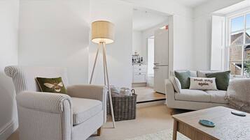 A modern living room with a striped armchair, a floor lamp, a sofa with green pillows, and a coffee table.