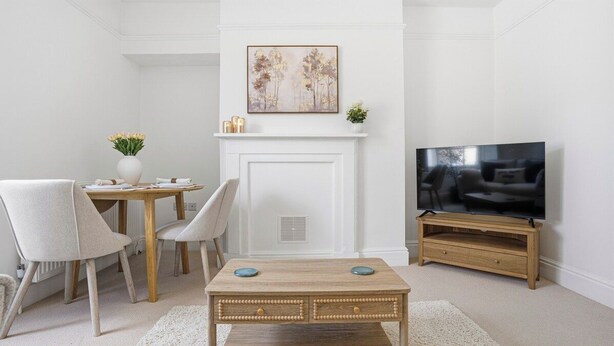 Uma sala de estar com lareira, televisão, mesa de jantar com cadeiras e mesa de centro.